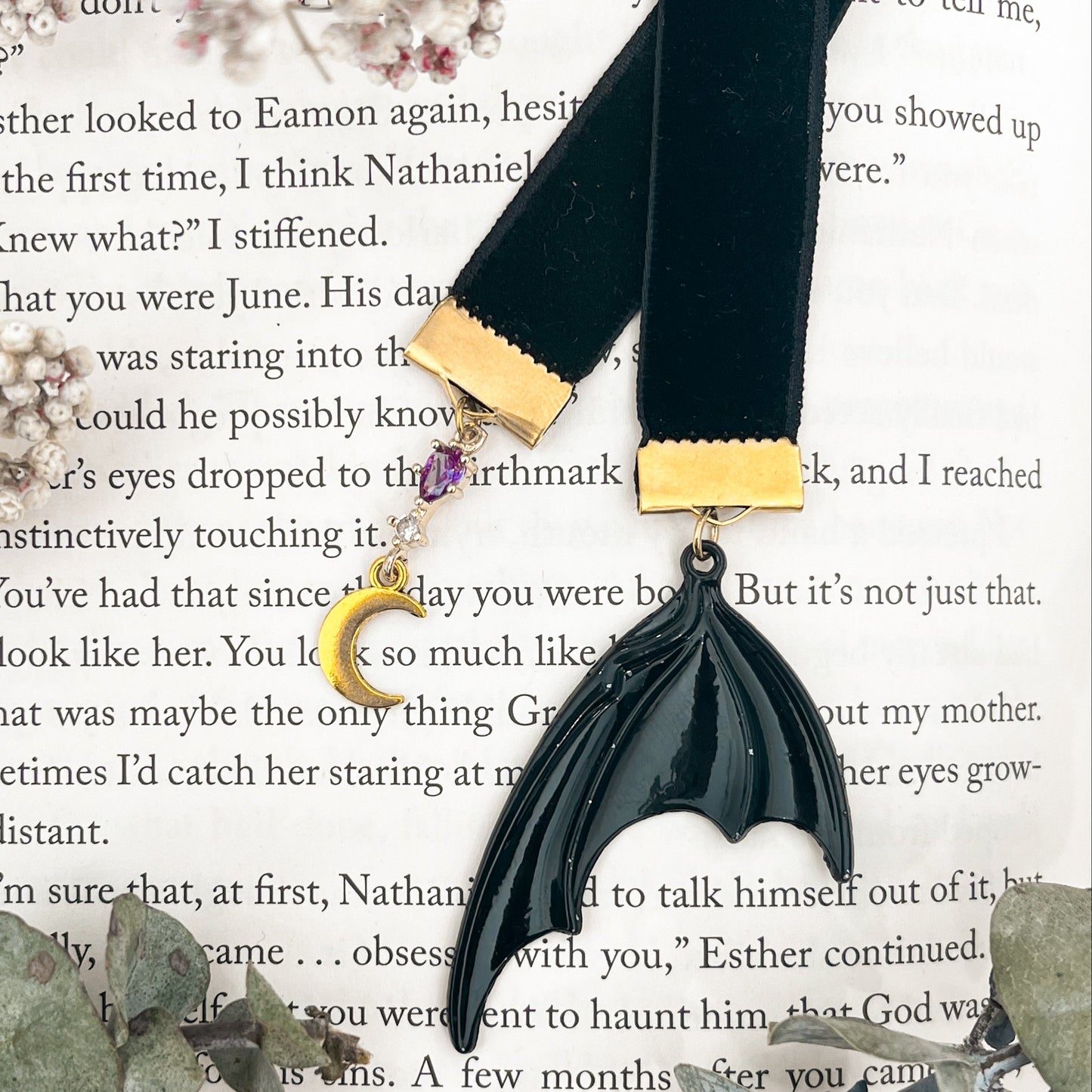 Black velvet ribbon bookmark with a purple gem and gold moon charm on one side and batwing on the other