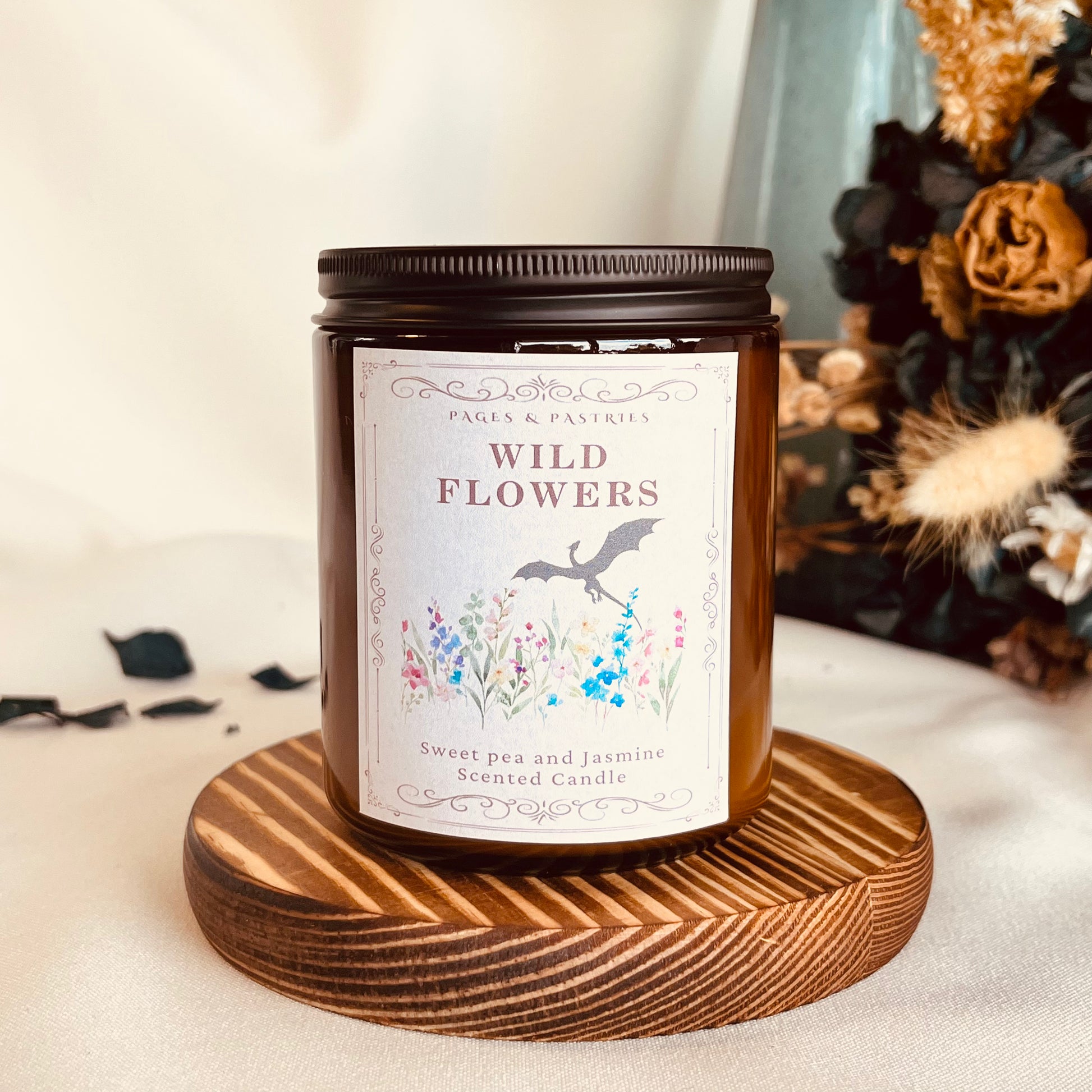 Wild Flowers bookish candle in amber glass jar with black lid, showing wyvern and wildflowers on label