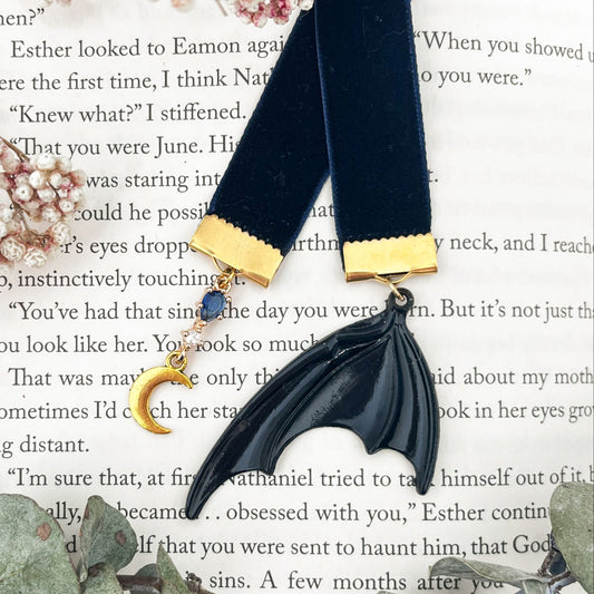 Blue velvet ribbon bookmark with a blue gem and moon on one end and a bat wing on the other