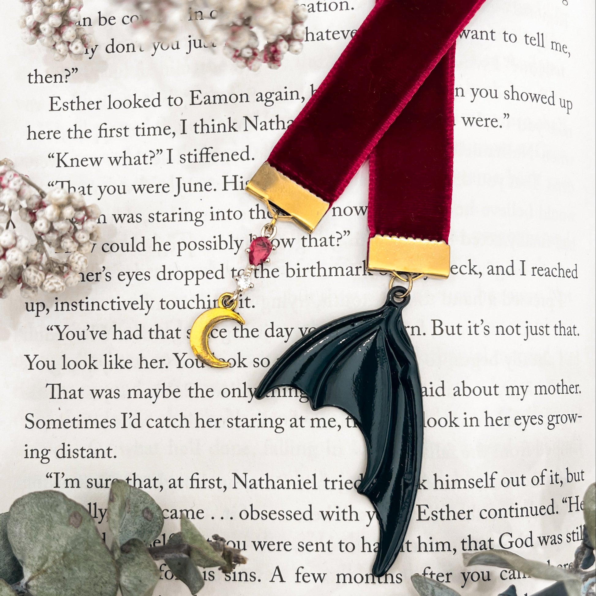 Black bat wing charm on a red ribbon with a red gem and moon charm on the other end