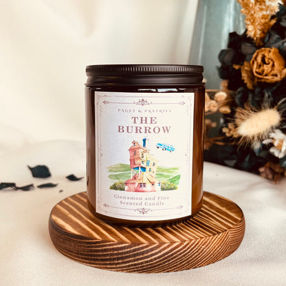 The Burrow bookish candle in amber glass jar with black lid, showing Weasley home and flying car label design