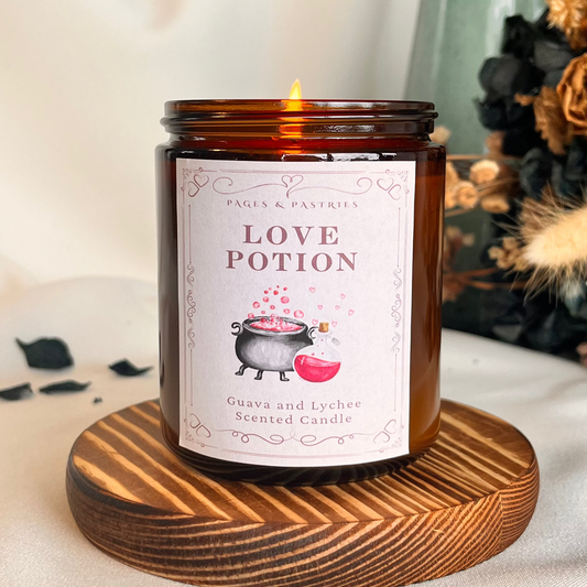Amber glass love potion candle with lychee and guava scent, bookish inspired label featuring a bubbling cauldron and pink potion bottle.