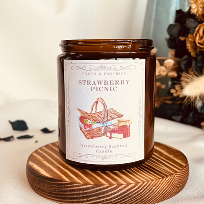 Strawberry Picnic bookish candle in amber glass jar with strawberry scent, featuring picnic basket and strawberries on label