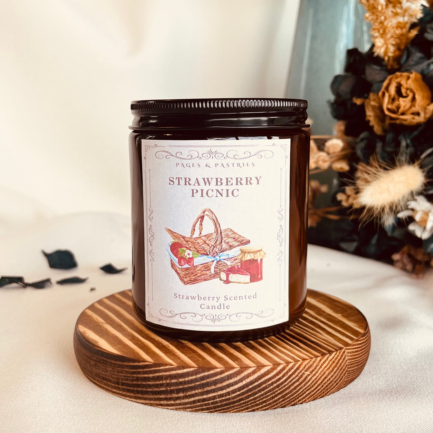 Strawberry Picnic bookish candle in amber glass jar with black lid, showing picnic basket and strawberries label design